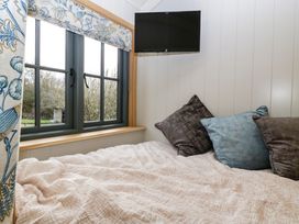 A bedroom corner with a bed covered in a beige quilt with pillows and a wall-mounted television near a window with floral curtains at Evendine Hut