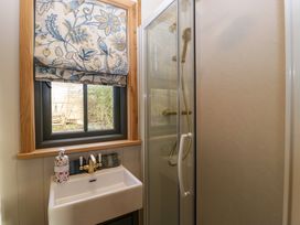 A bathroom with a white sink brass faucet floral soap dispenser glass shower enclosure and a window with floral Roman shade at Evendine Hut @ Evendine Cottage Colwall Herefordshire