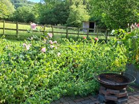A garden with flowers, a grill and a shed at Evendine Hut @ Evendine Cottage, Colwall, Herefordshire