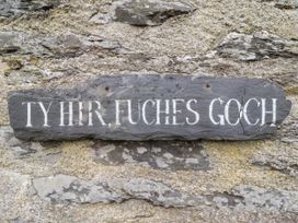 A stone wall with a dark slate sign reading Ty Hir Fuches Goch at The Long House in Penmachno