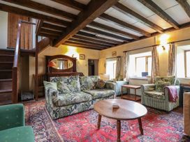 A living room with floral and striped armchairs a wooden coffee table and a red patterned rug at The Long House in Penmachno