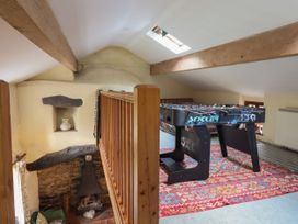 An upper loft area with a foosball table on a patterned rug and wooden beams at The Long House in Penmachno