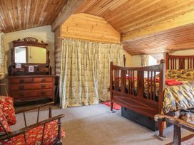 A bedroom with wooden ceiling a bed a dresser with mirror and floral curtains at The Long House in Penmachno