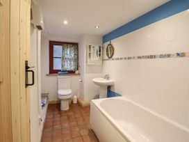 A bathroom with a bathtub a sink a toilet a small mirror and a window with floral curtain at The Long House in Penmachno