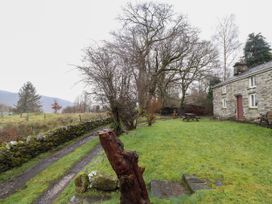 A grassy yard with a stone cottage picnic table trees and stone fence at The Long House in Penmachno
