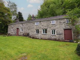 A stone house with a bench and grass area at The Long House in Penmachno