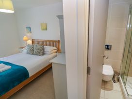 A bedroom with a wooden bed and pillows next to a bedside table lamp and an adjacent bathroom with a toilet and glass shower at Talland View in St Ives