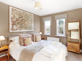 A bedroom with a bed with pillows and folded towels on it two bedside tables with lamps two windows with striped blinds and a wooden dresser with a mirror at Thorncliffe House in Pocklington