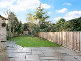 A backyard with a stone patio, grass lawn, trees, wooden fence, and a small shed at Thorncliffe House in Pocklington