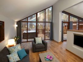 A living room with armchairs a sofa pillows a coffee table and large windows overlooking a deck with hot tub at Thorpe Forest Silver Birch in Thorpe Forest