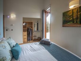 A bedroom with a bed a wooden wardrobe hanging robes and a window with a view of trees at Thorpe Forest Silver Birch in Thorpe Forest