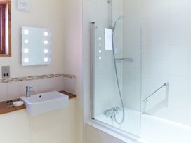 A bathroom with a sink a mirror with lights a bathtub with a glass shower screen and a showerhead at Thorpe Forest Silver Birch in Thorpe Forest