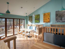 A dining area with wooden tables chairs and cushioned benches near large glass doors with outdoor seating at Delamere Forest Silver Birch Delamere Forest