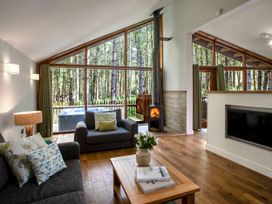 A living room with large windows showing trees outside two sofas a coffee table with books and flowers and a wood burning stove at Thorpe Forest Golden Oak in Thorpe Forest