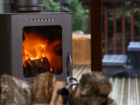 A burning wood stove with logs in front and a view of a deck outside at Thorpe Forest Golden Oak in Thorpe Forest