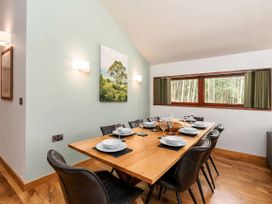 A dining room with a wooden table set for eight and a window showing trees outside at Strathyre New Style Golden Oak in Strathyre Ben Ledi