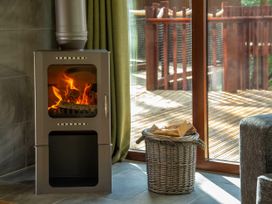 A wood burning stove with firewood in a basket beside a sliding glass door on a tiled floor at Strathyre New Style Golden Oak in Strathyre, Ben Ledi