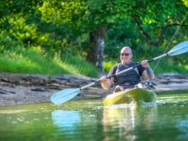 A man paddling a kayak on a river near a grassy and wooded riverbank at Ardgartan Argyll Golden Oak in Ardgartan Loch Long