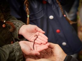 Two people holding an earthworm in their hands outdoors
