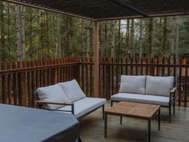 An outdoor wooden deck with two cushioned sofas and a wooden table surrounded by a wooden railing at Glentress The Unfurl Cabin in Glentress Forest Peebles