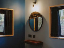 A corner wall with a round mirror a small wooden shelf and two windows with black curtains at Glentress The Unfurl Cabin (2 doubles 1 twin) in Glentress Forest Peebles