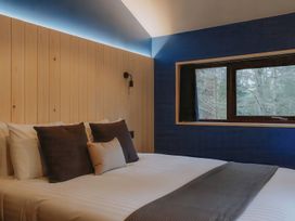 A bedroom with a bed with multiple pillows a wooden headboard and a window showing trees at Glentress The Unfurl Cabin 2 doubles 1 twin in Glentress Forest Peebles