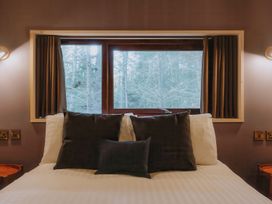 A bed with dark pillows and white sheets in front of a window with curtains at Glentress The Unfurl Cabin 2 doubles 1 twin in Glentress Forest Peebles
