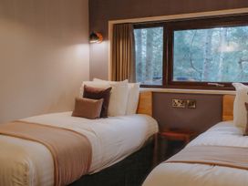 A bedroom with two single beds with pillows and blankets a window and a small table at Glentress The Unfurl Cabin 2 doubles 1 twin in Glentress Forest Peebles