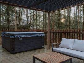 An outdoor covered deck with a hot tub sofa and table surrounded by trees at Glentress The Unfurl Cabin (2 doubles 1 twin) in Glentress Forest Peebles