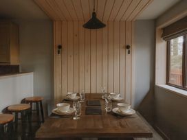 A dining table set with bowls, plates, cutlery, and glasses in a room with wooden walls and stools by a counter at Glentress The Unfurl Cabin in Glentress Forest, Peebles