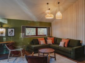 A living room with a green sectional sofa, wooden chairs, a round wooden coffee table, and pendant lights at Glentress The Unfurl Cabin (2 doubles 1 twin) in Glentress Forest Peebles