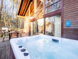 An outdoor deck with a hot tub wooden table and chairs and a wooden cabin with large glass windows at Keldy Classic Silver Birch in Keldy Forest