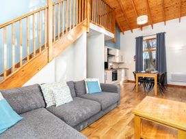 A living room with a gray sofa and wooden staircase and dining table with chairs near a kitchen at Keldy Classic Silver Birch in Keldy Forest
