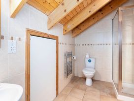 A bathroom with a toilet a shower enclosure a small sink and a door under a slanted wooden ceiling at Keldy Classic Silver Birch in Keldy Forest
