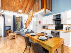 An open plan living and dining area with wooden dining table and chairs kitchen with white cabinets and black appliances grey sofa and wooden coffee table under a wooden vaulted ceiling at Keldy Classic Silver Birch in Keldy Forest