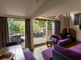 A living room with purple sofas a wood stove and large glass doors opening to a deck with outdoor furniture at Deerpark Classic Golden Oak Treehouse in Deerpark Forest