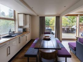 A kitchen and dining area with a wooden table and benches by large windows overlooking a deck at Deerpark Classic Golden Oak Treehouse in Deerpark Forest