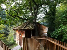 A wooden treehouse with a walkway railing surrounded by trees at Deerpark Classic Golden Oak Treehouse in Deerpark Forest