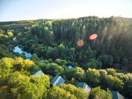 A forest with tall trees a pond and rooftops of houses surrounded by greenery at Deerpark Classic Golden Oak Treehouse in Deerpark Forest