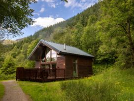 A wooden cabin with a metal roof and fenced deck surrounded by trees and grass at Strathyre Classic Golden Oak Strathyre Ben Ledi