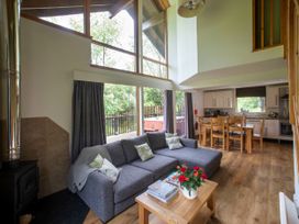 A living room with a gray sofa and wooden coffee table with flowers and books next to a dining table and kitchen at Strathyre Classic Golden Oak Strathyre Ben Ledi