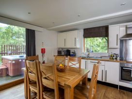 A kitchen with wooden dining table and chairs next to a window and sliding glass door showing a hot tub at Strathyre Classic Golden Oak in Strathyre Ben Ledi