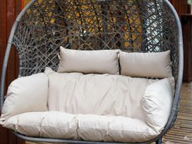 A cushioned outdoor hanging chair with a woven frame on a wooden deck at Strathyre Golden Oak Hideaway Strathyre Ben Ledi