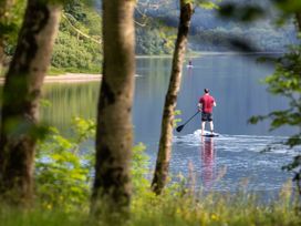 A person paddleboarding on a calm lake surrounded by trees at Strathyre Golden Oak Hideaway Strathyre Ben Ledi