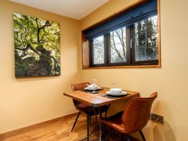 A small dining area with a wooden table set for two and two brown chairs next to a window with blue blinds and a tree photograph on the wall at Strathyre Golden Oak Hideaway in Strathyre Ben Ledi