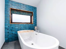 A bathroom with a white freestanding bathtub against a blue tiled wall and a window above with a patterned blind at Strathyre Golden Oak Hideaway Strathyre Ben Ledi