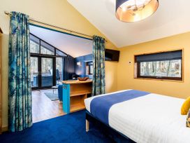 A bedroom with a bed and blue carpet leading to a living area with glass doors and blue curtains at Strathyre Golden Oak Hideaway in Strathyre Ben Ledi