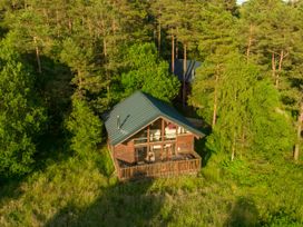 A wooden cabin with a fenced porch surrounded by trees and grass at Keldy Classic Golden Oak in Keldy Forest