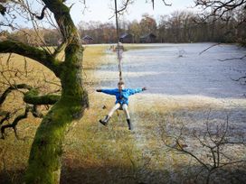 A child swinging on a zip line surrounded by a grassy field and wooden cabins in the background at Keldy Classic Golden Oak Keldy Forest
