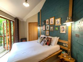 A bedroom with a large bed and framed pictures on a blue wooden wall at Forest of Dean Woodland - Golden Oak Treehouse in Forest Of Dean